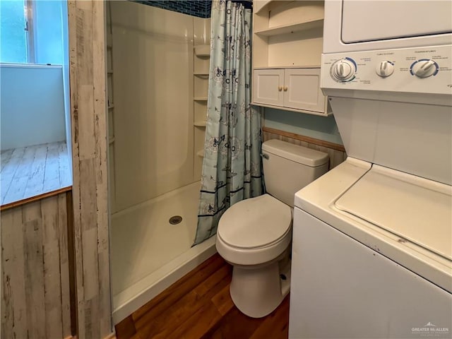 bathroom featuring stacked washer and dryer, toilet, wood finished floors, and a stall shower