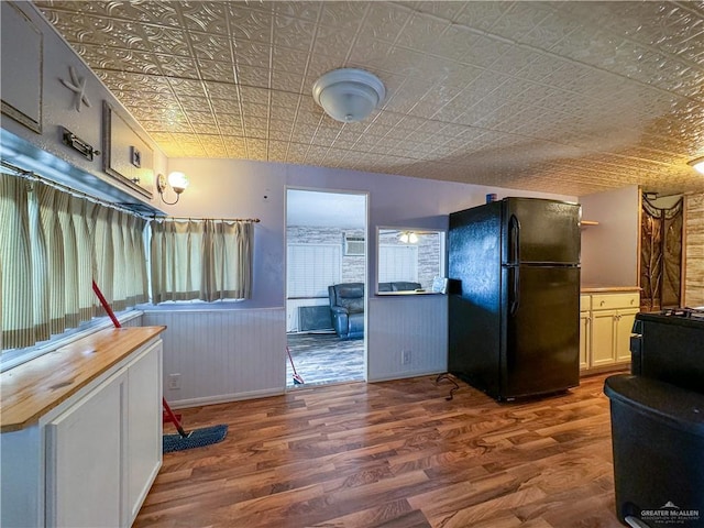 kitchen with wood finished floors, a wainscoted wall, an ornate ceiling, freestanding refrigerator, and butcher block counters