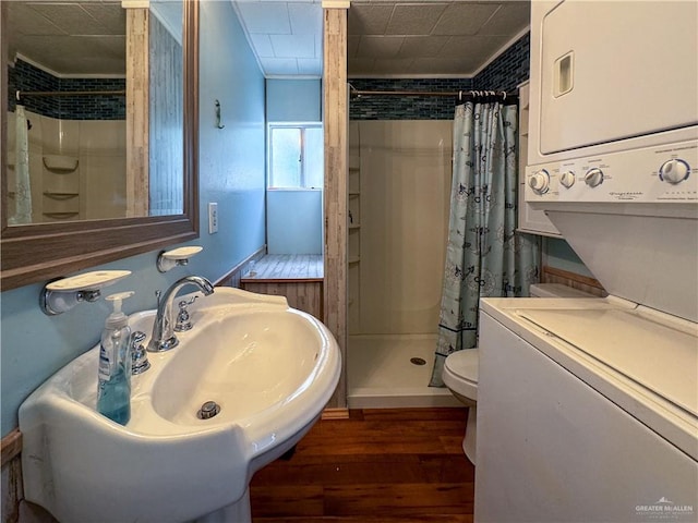 full bathroom with toilet, ornamental molding, stacked washer and dryer, a stall shower, and wood finished floors