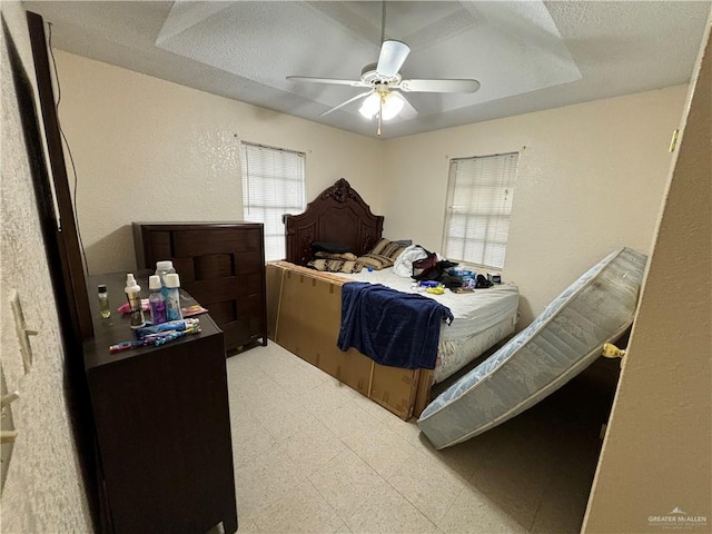 bedroom with ceiling fan, a textured ceiling, and a tray ceiling