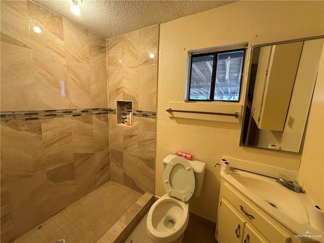 bathroom with vanity, toilet, tiled shower, and a textured ceiling