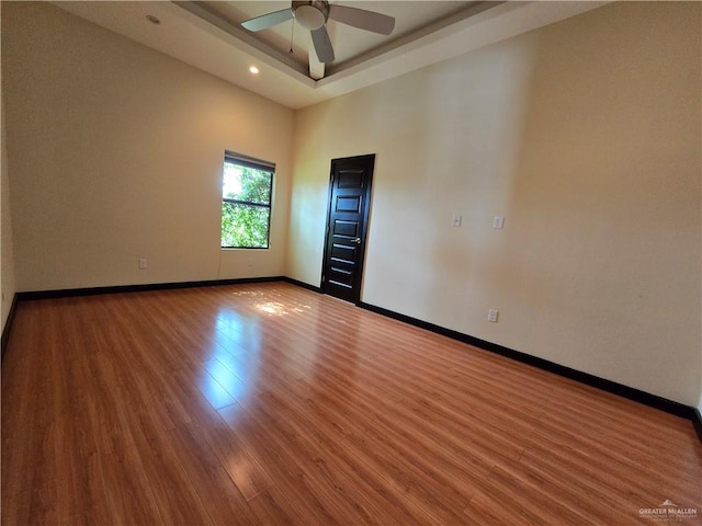 unfurnished room with ceiling fan, a raised ceiling, hardwood / wood-style floors, and a high ceiling