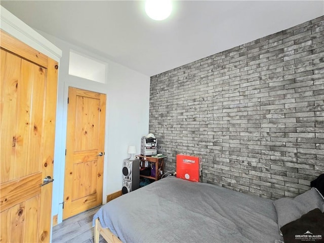 bedroom with brick wall and hardwood / wood-style floors