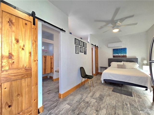 bedroom with wood-type flooring, a barn door, a wall mounted air conditioner, and ceiling fan