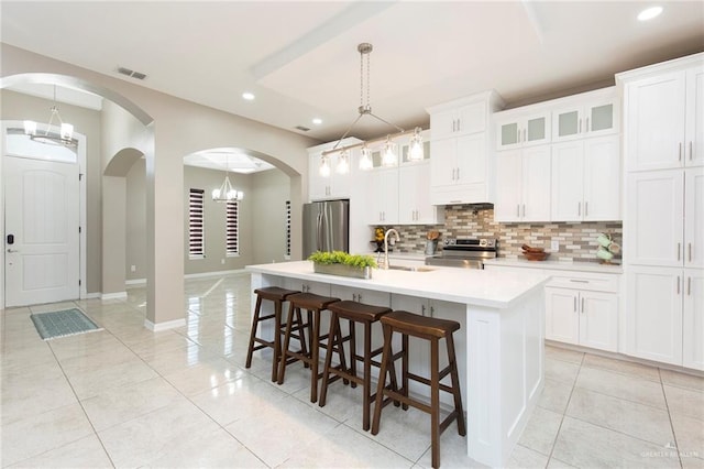 kitchen with sink, white cabinetry, hanging light fixtures, stainless steel appliances, and a center island with sink