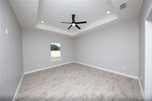 unfurnished room with a raised ceiling, ceiling fan, and light hardwood / wood-style flooring