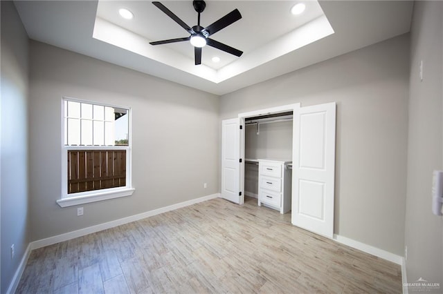 unfurnished bedroom featuring a closet, a raised ceiling, ceiling fan, and light hardwood / wood-style flooring