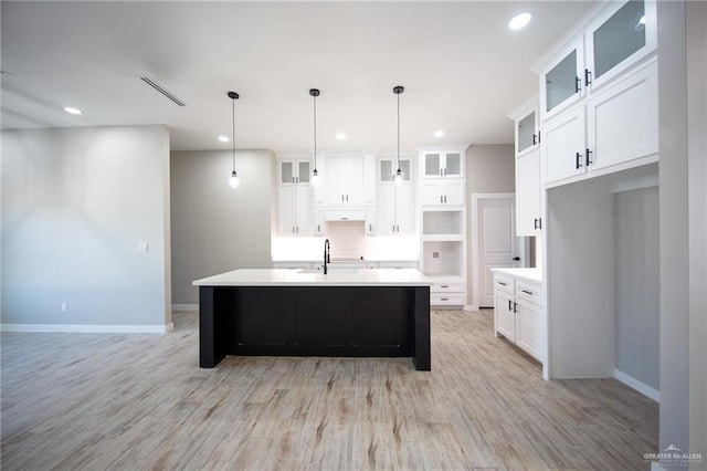 kitchen with a kitchen island with sink, white cabinets, and decorative light fixtures