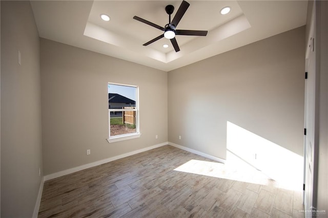 spare room with a tray ceiling, hardwood / wood-style flooring, and ceiling fan