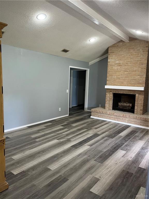 1601 S Oklahoma Ave, Weslaco, TX 78596 - unfurnished living room featuring a textured ceiling, wood finished floors, and a brick fireplace