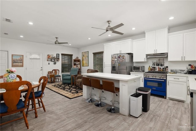 kitchen with appliances with stainless steel finishes, ceiling fan, white cabinets, light hardwood / wood-style floors, and a kitchen island