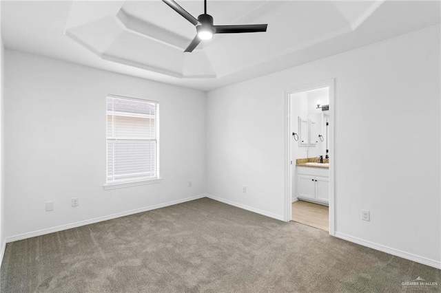 unfurnished bedroom featuring ceiling fan, a raised ceiling, light carpet, and connected bathroom