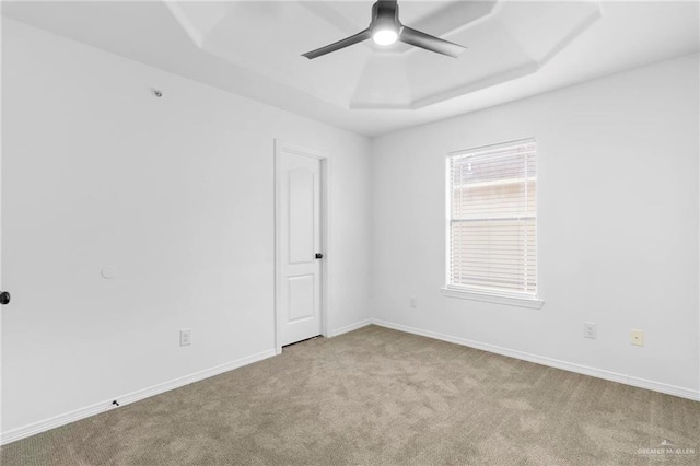 empty room with light carpet, a tray ceiling, and ceiling fan