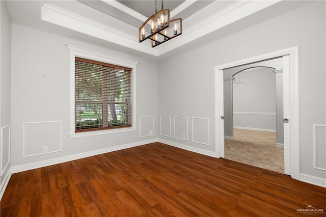 empty room with a raised ceiling, crown molding, dark hardwood / wood-style flooring, and an inviting chandelier