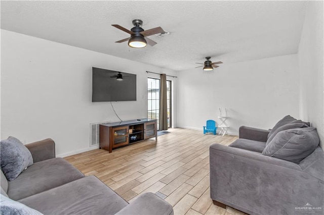 living room featuring visible vents, baseboards, light wood-style floors, and a textured ceiling