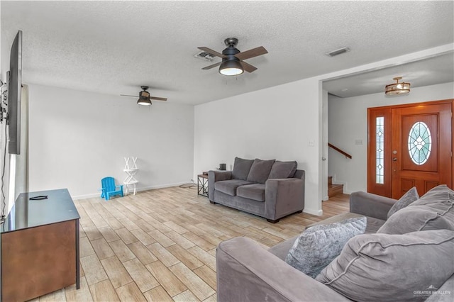 living room with visible vents, ceiling fan, stairs, light wood-type flooring, and a textured ceiling