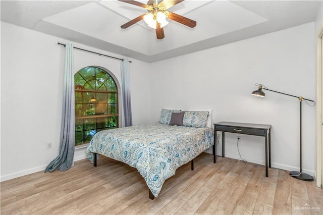 bedroom featuring a raised ceiling, light wood-style flooring, a ceiling fan, and baseboards