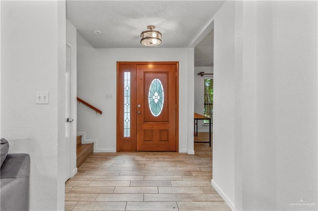 entryway with a wealth of natural light, baseboards, a textured ceiling, and wood tiled floor