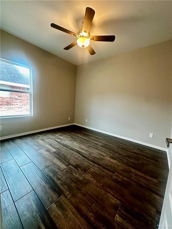 spare room featuring dark wood finished floors, a ceiling fan, and baseboards