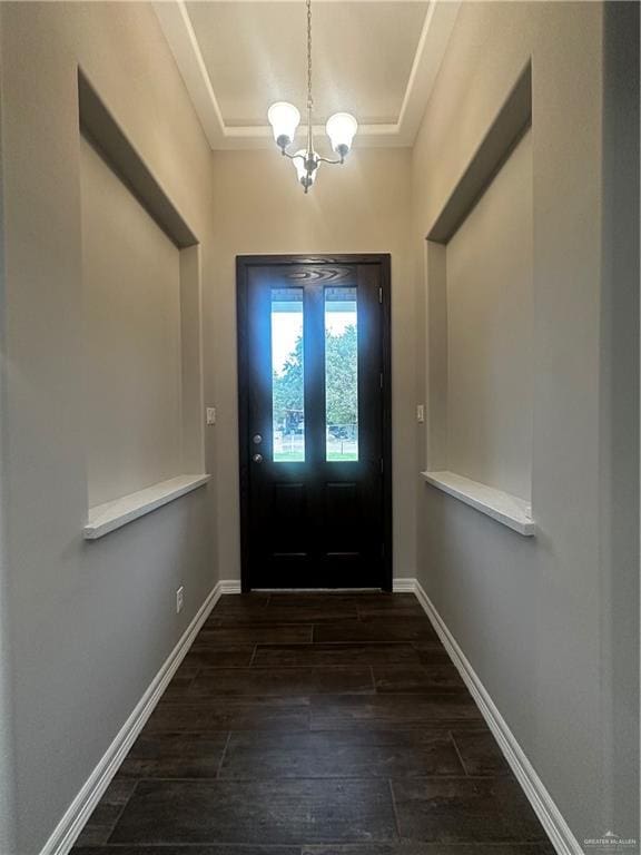 entrance foyer with a chandelier, a tray ceiling, wood finished floors, and baseboards