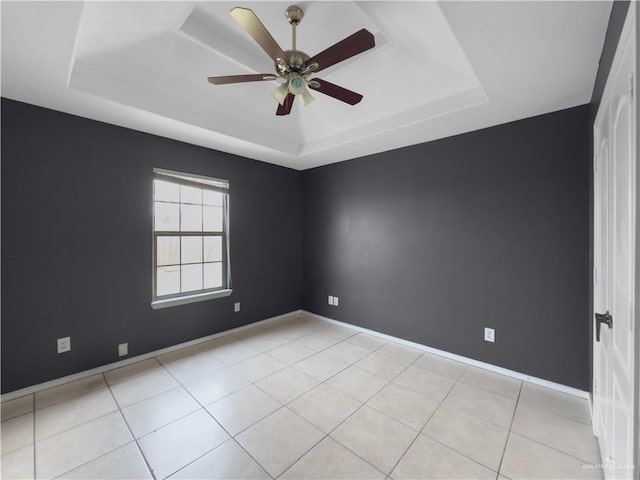 unfurnished room with light tile patterned floors, baseboards, ceiling fan, and a tray ceiling