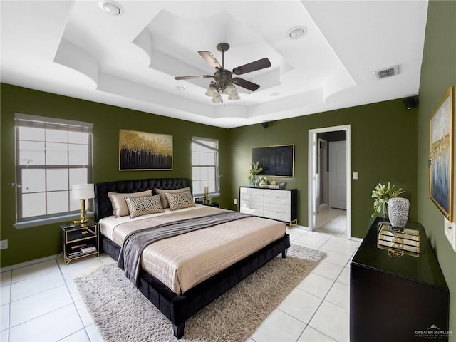 bedroom featuring a ceiling fan, visible vents, light tile patterned floors, baseboards, and a tray ceiling