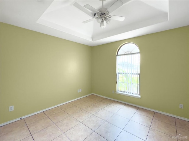 empty room featuring a ceiling fan, baseboards, light tile patterned floors, and a raised ceiling