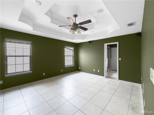 spare room featuring a raised ceiling, baseboards, a ceiling fan, and visible vents