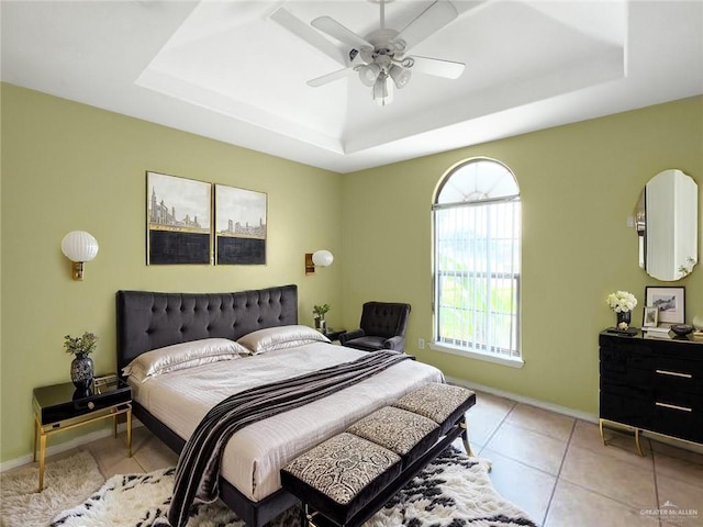 bedroom featuring baseboards, ceiling fan, light tile patterned floors, and a tray ceiling