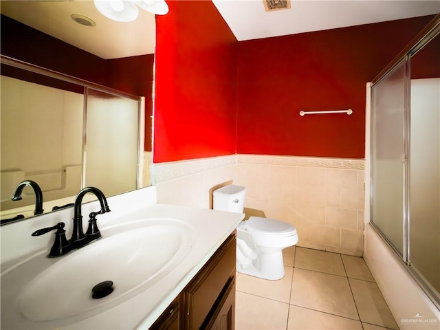bathroom with tile patterned flooring, vanity, toilet, a wainscoted wall, and tile walls