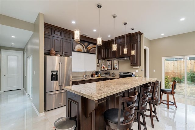 kitchen with a kitchen breakfast bar, hanging light fixtures, light stone countertops, dark brown cabinetry, and stainless steel appliances