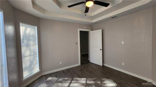 spare room featuring ceiling fan, dark hardwood / wood-style floors, a raised ceiling, and a healthy amount of sunlight