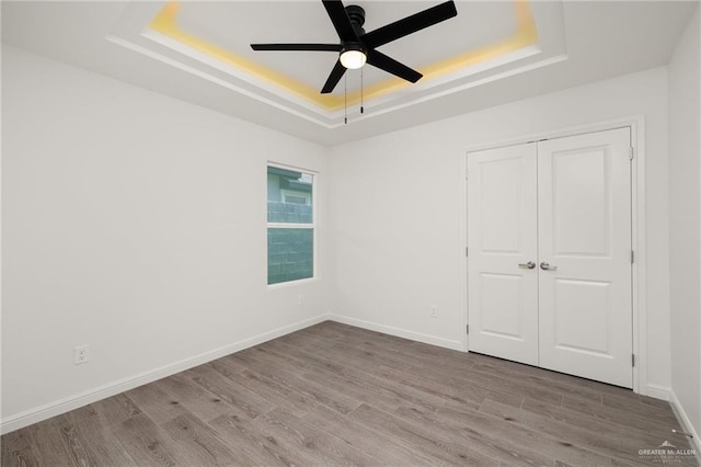 unfurnished bedroom with ceiling fan, a raised ceiling, a closet, and light wood-type flooring