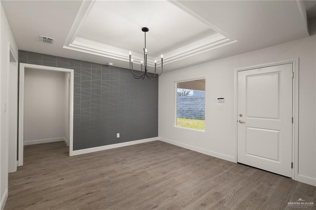 unfurnished dining area with an inviting chandelier, wood-type flooring, a raised ceiling, and tile walls