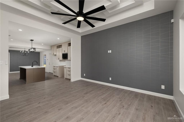 unfurnished living room featuring a raised ceiling, sink, and dark wood-type flooring