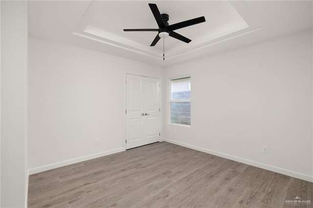 empty room featuring ceiling fan, a raised ceiling, and light wood-type flooring