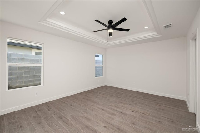 empty room featuring a raised ceiling, hardwood / wood-style flooring, and ceiling fan