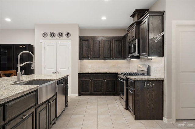 kitchen with a sink, decorative backsplash, light tile patterned floors, appliances with stainless steel finishes, and light stone countertops