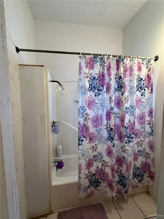 bathroom with tile patterned floors, shower / bath combo with shower curtain, and a textured ceiling