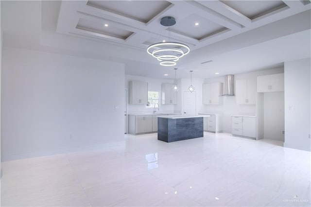 kitchen with coffered ceiling, wall chimney range hood, a center island, white cabinetry, and hanging light fixtures