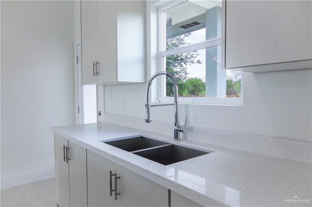 kitchen featuring light stone countertops, white cabinets, and sink