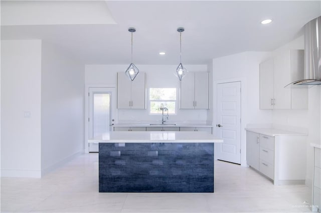 kitchen with wall chimney exhaust hood, sink, white cabinets, a kitchen island, and hanging light fixtures