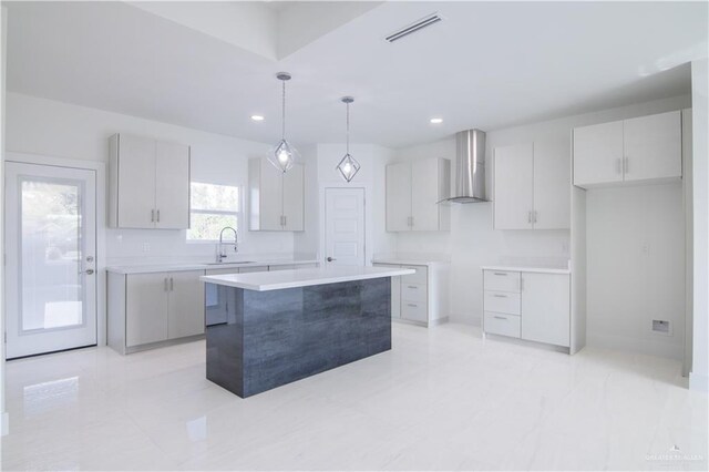 kitchen with sink, wall chimney exhaust hood, a kitchen island, decorative light fixtures, and white cabinets