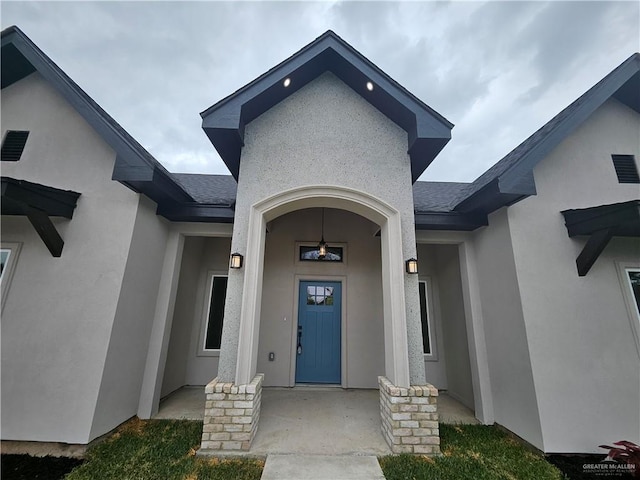 entrance to property featuring stucco siding and roof with shingles