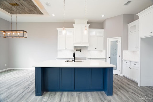 kitchen with pendant lighting, sink, backsplash, and a kitchen island with sink