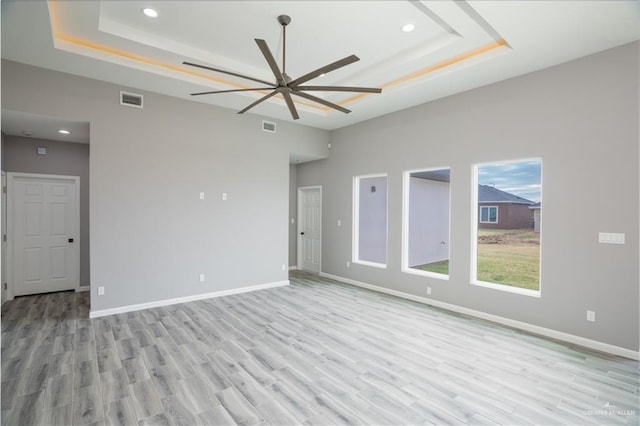 empty room featuring ceiling fan, a towering ceiling, light wood-type flooring, and a tray ceiling