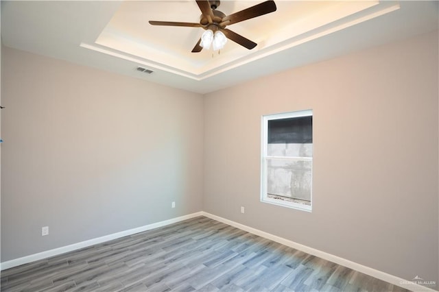 empty room with ceiling fan, wood-type flooring, and a tray ceiling