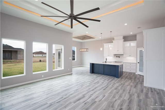 kitchen with sink, a kitchen island with sink, decorative backsplash, white cabinets, and decorative light fixtures