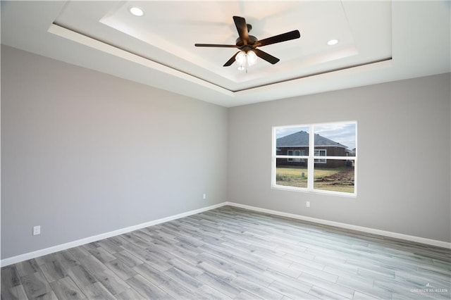 spare room with a tray ceiling, light hardwood / wood-style floors, and ceiling fan