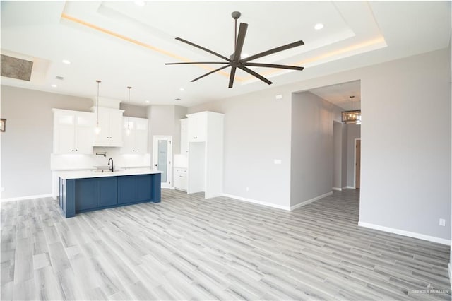 kitchen with decorative light fixtures, white cabinets, light hardwood / wood-style floors, a tray ceiling, and a center island with sink